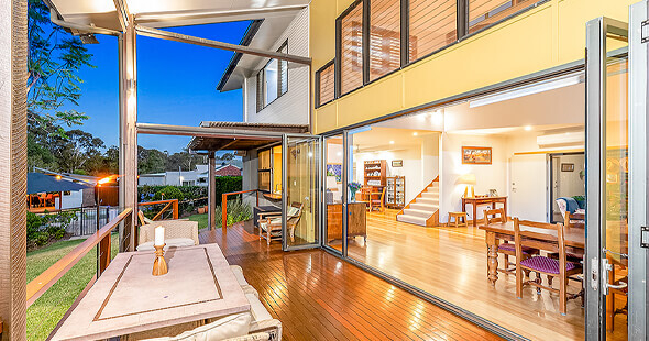 Looking into a two storey house from the patio late at dusk with lights on